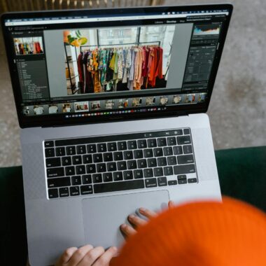 A person in a cozy setting edits photos of clothing displays on a laptop.